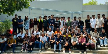 Large group of young people posing outdoors on steps under a clear sky.