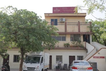 A two-story building with vehicles and trees in front, labeled Aaytan Academy.