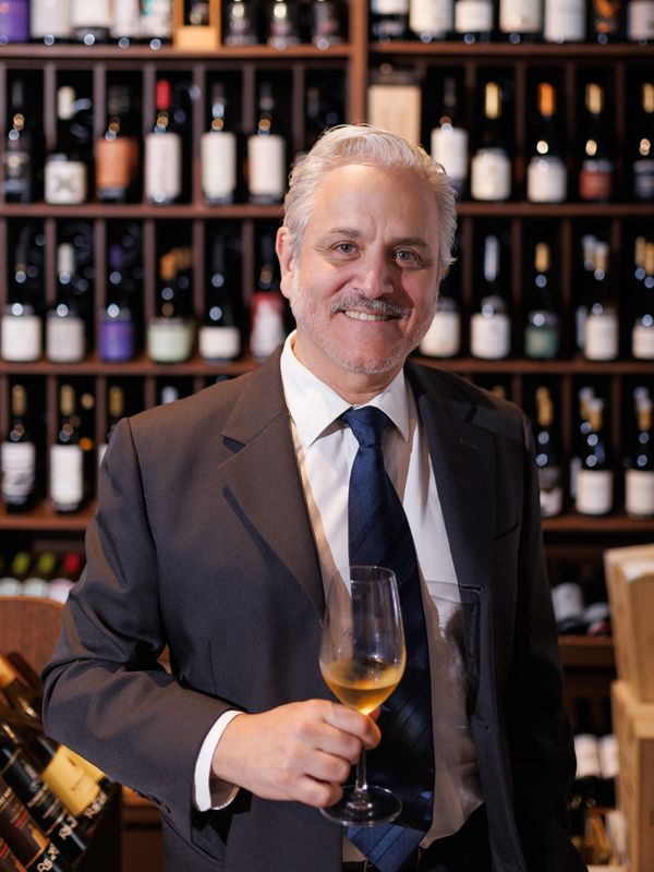 Homem de terno segurando uma taça de vinho branco.