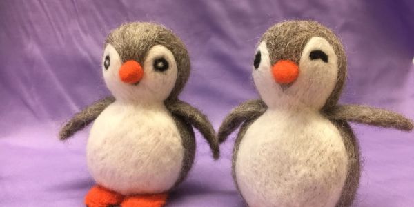 Two cute felt penguin figurines on purple background.