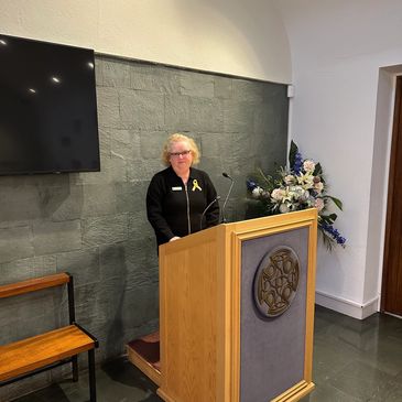 Woman standing at a wooden podium with a mic and flowers.
