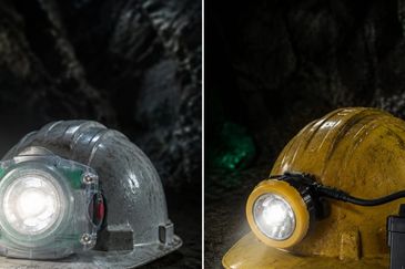 Two mining helmets with bright LED lamps in a dark underground setting.