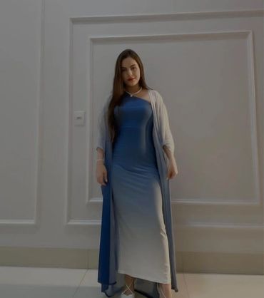 karachi escorts in a blue and white gradient gown with a sheer shawl stands against a white paneled