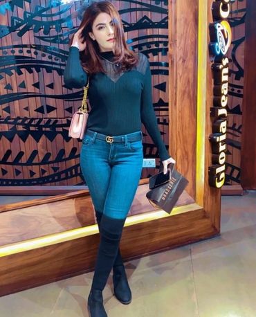 call girl in karachi in black top and jeans posing indoors with shopping bags.