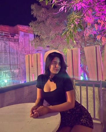 A young dha escorts karachi sitting at a table with colorful night lights and trees in the background.