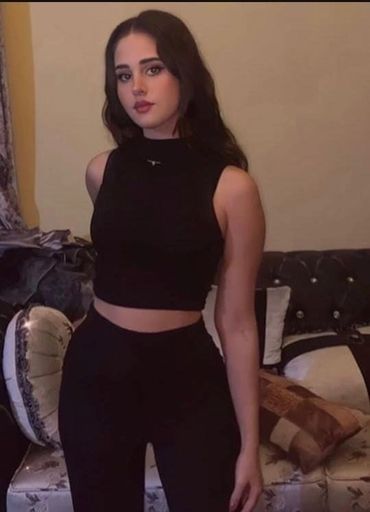 A young Escorts in Karachi in a black sleeveless crop top and pants poses indoors.