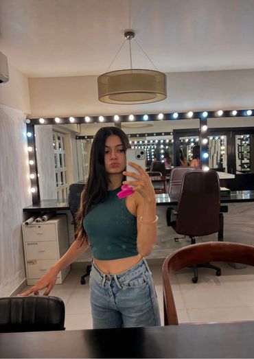 Young call girl karachi taking a mirror selfie in a well-lit room with vanity lights.