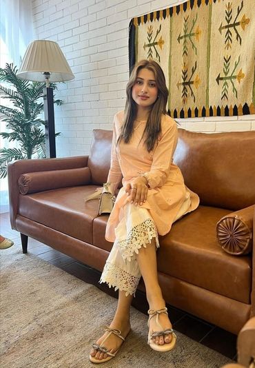 karachi escorts in traditional attire sitting on a brown leather couch indoors.