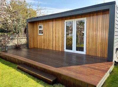 Modern wooden garden shed with a dark wood deck and glass doors.