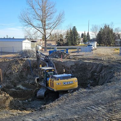 A yellow Deere excavator digging a deep hole at a construction site.