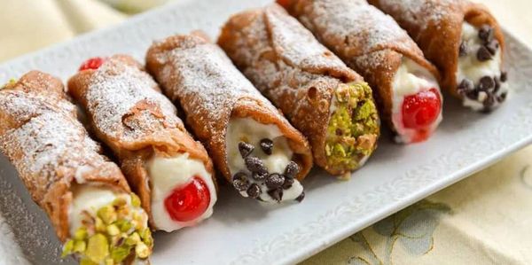 A plate of assorted cannoli with creamy filling, pistachios, chocolate chips, and cherries.