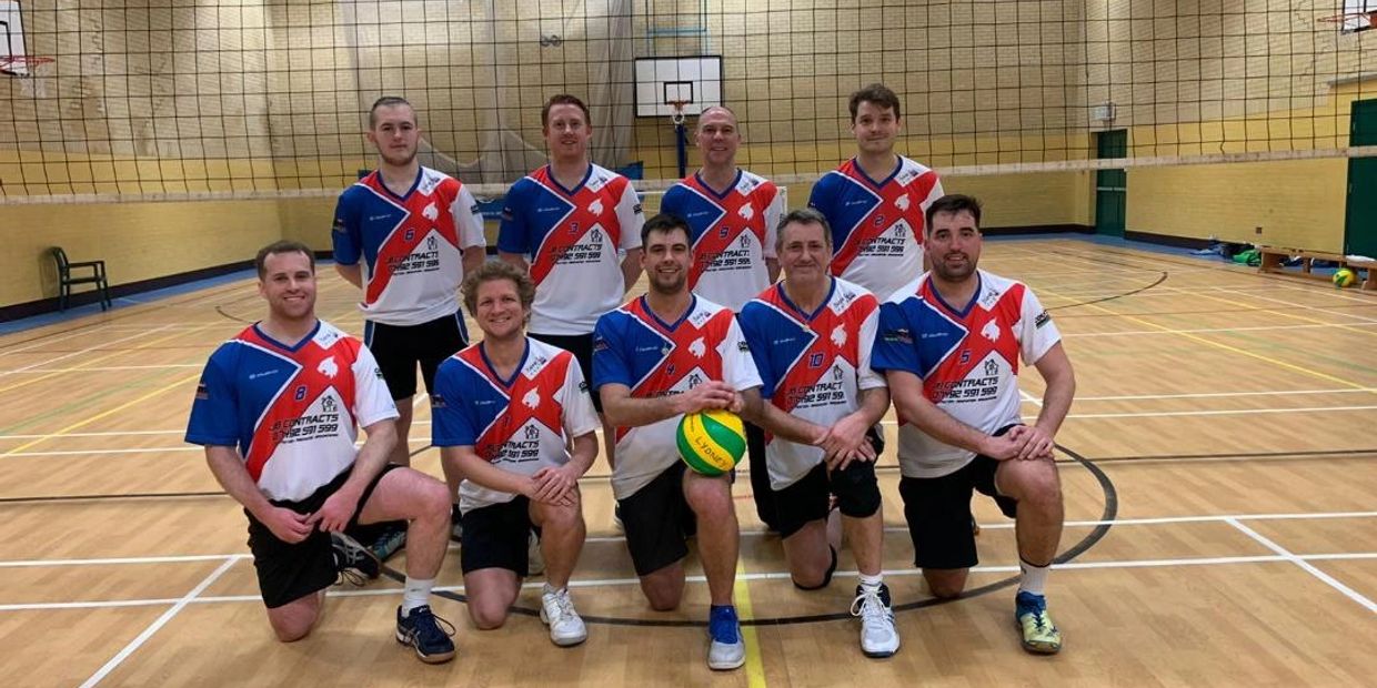 Volleyball team posing in gym with their uniforms and volleyball.