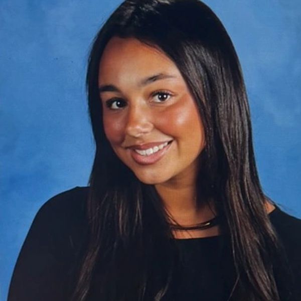 Smiling young woman with long dark hair and a black top against a blue background.