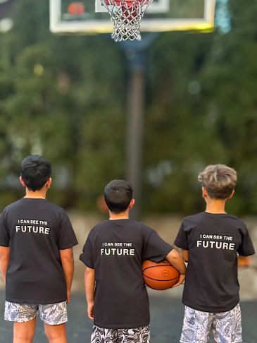 Three boys in matching shirts holding a basketball under a hoop.