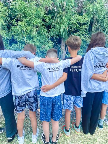 A group of young friends wearing shirts with motivational phrases, standing side by side with arms around each other.