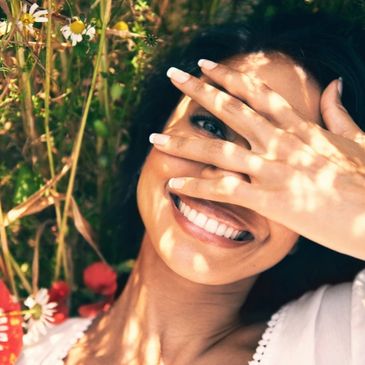 Joyful mom playfully peeking through her fingers, surrounded by vibrant flowers.
