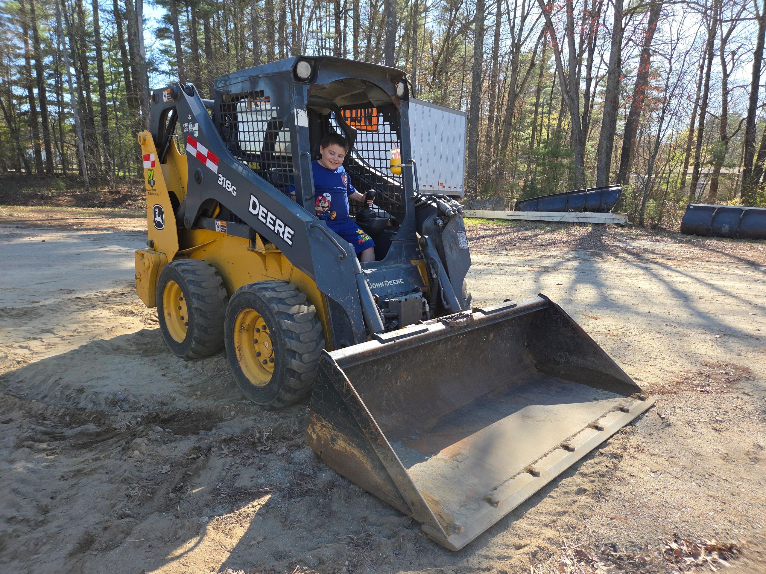 A child joyfully operating a John Deere skid steer loader outdoors.