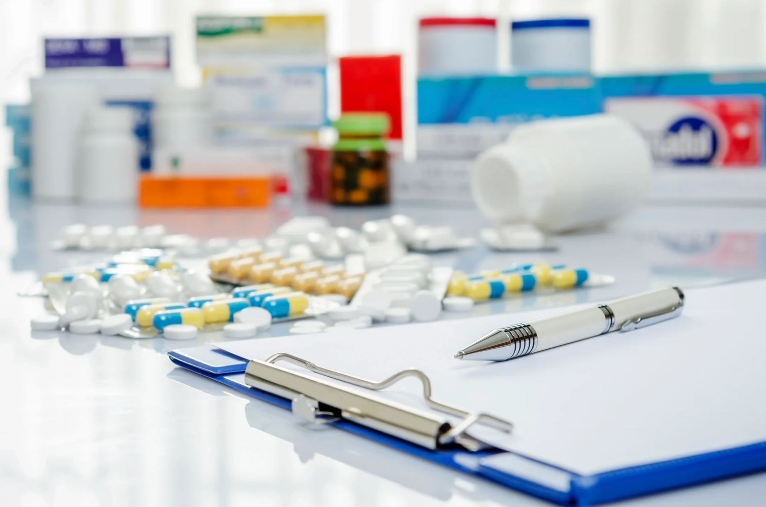 Medical clipboard with pen and various medications scattered on a white surface.