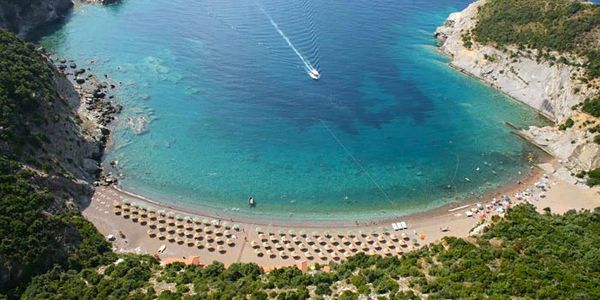 Aerial view of a tranquil beach with umbrellas and a boat in clear blue water.