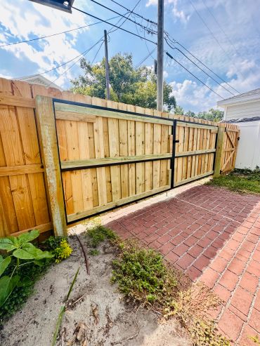 Wooden fence gate with a brick driveway.