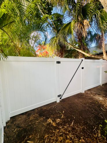 White vinyl fence with tropical plants behind it.