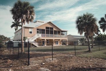 Two-story house with a screened porch and palm trees.