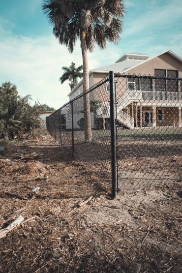 House behind a black chain-link fence with palm trees.