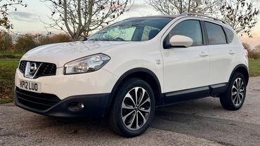 White Nissan SUV parked on a paved road with trees in the background.
