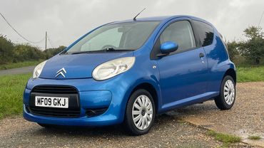 Blue Citroën compact car parked on a gravel road under an overcast sky.
