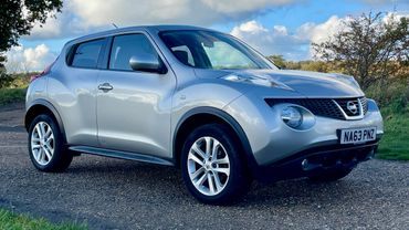 Silver Nissan Juke parked on a rural road under a partly cloudy sky.