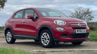 Red Fiat 500X parked on a gravel path under a cloudy sky.