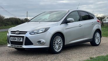 Silver Ford hatchback parked on a rural road under a cloudy sky.