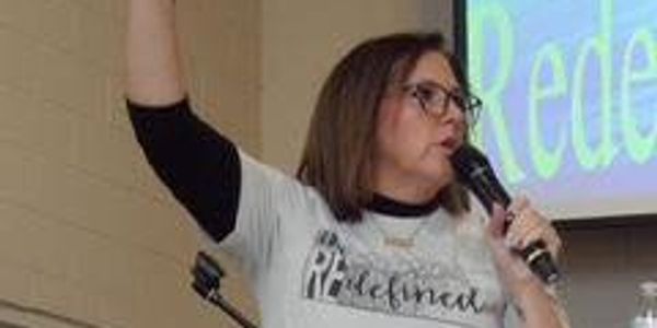 Woman speaking into a microphone with a raised arm during a presentation.
