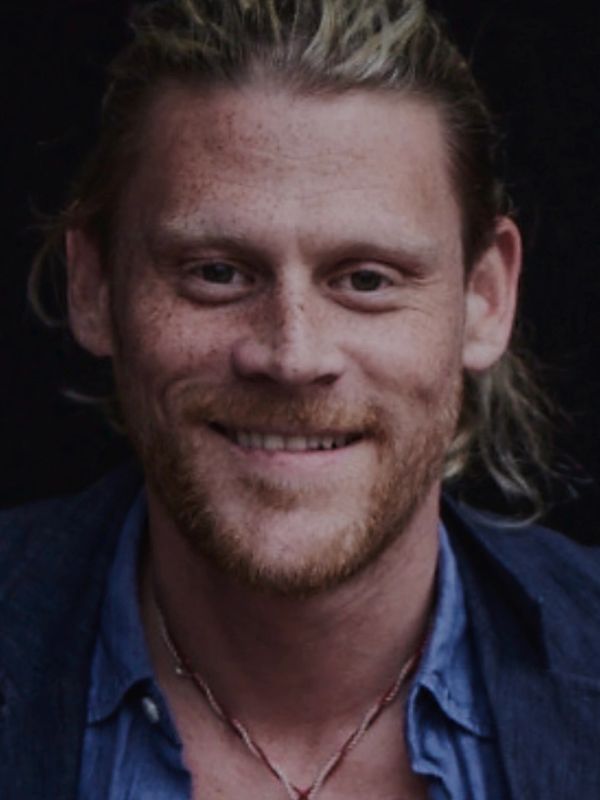 Smiling man with red beard and necklace.