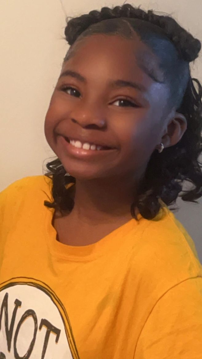 Smiling girl in a yellow shirt with curly hair tied up.