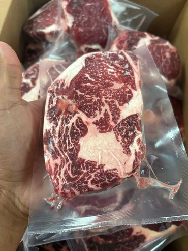 Hand holding vacuum-sealed marbled beef steak.