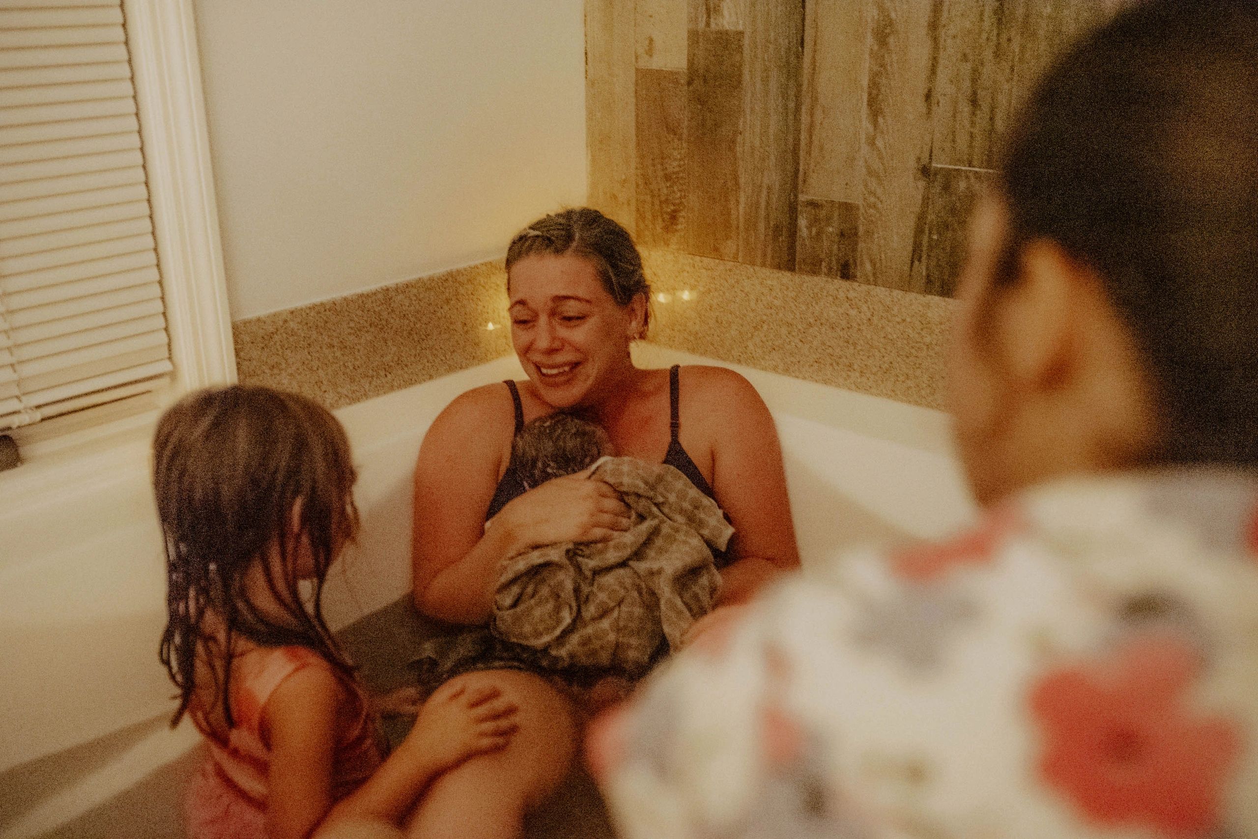 mother smiles at older child while holding newborn in birth pool
