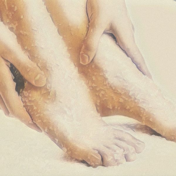 Hands applying salt scrub to feet for exfoliation.
