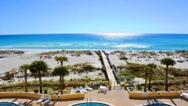 Sunny beach with clear blue water and a boardwalk leading to the shore.