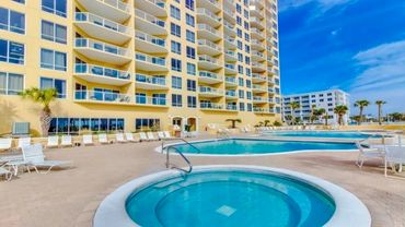 Sunny view of a resort pool area with lounge chairs and tall buildings.