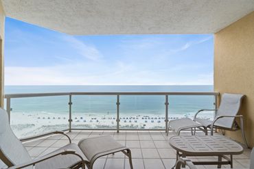 Balcony with chairs overlooking a serene beach and ocean.
