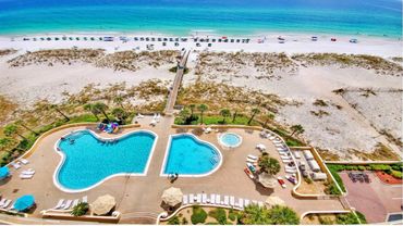 Aerial view of a beachside pool area with clear blue water and sandy beach.