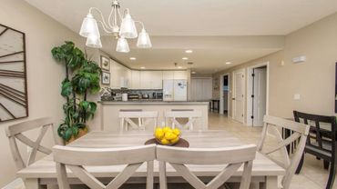 Modern dining area with light wood furniture and a bright kitchen in the background.