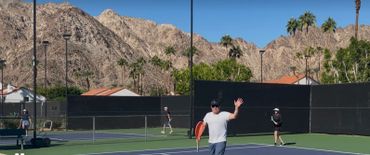 People playing pickleball on outdoor courts with mountains in the background.