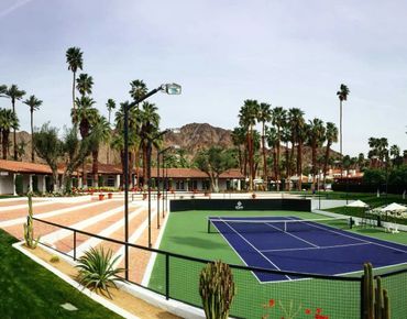 A tennis court surrounded by palm trees and desert mountains.