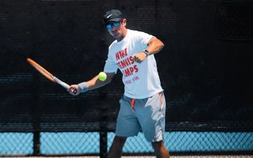 Man in white shirt and gray shorts playing tennis with a racket.