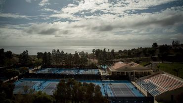 Tennis courts with ocean view under a cloudy sky.