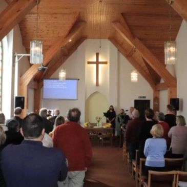 Congregation gathered in a church with wooden beams and a cross.