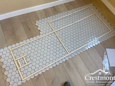Hexagonal tiles arranged on wooden floor with wooden sticks outlining a design.