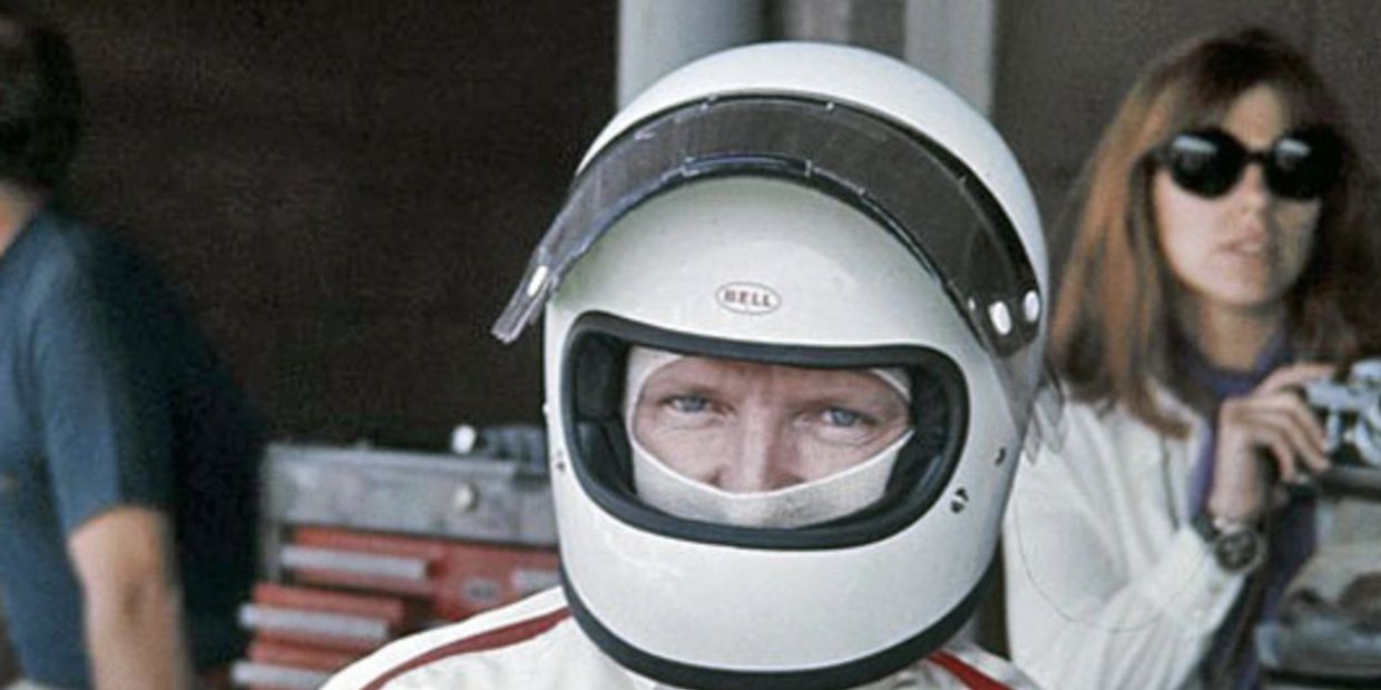 A race car driver wearing a white Bell helmet and suit.
